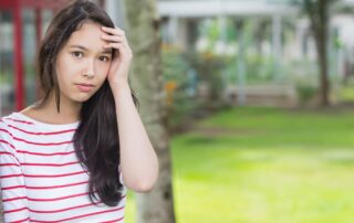 Teen girl looks thoughtful and anxious outdoors, representing the emotional impact of school anxiety.